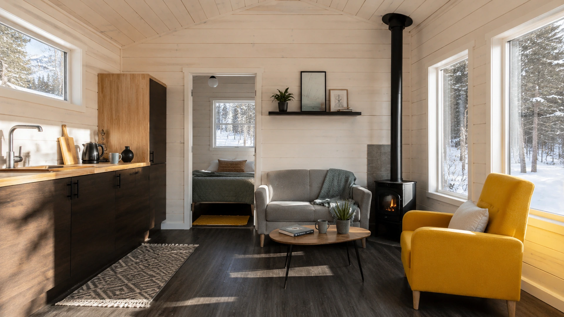 Tiny-home living room with a stove, kitchen and large woodland windows.