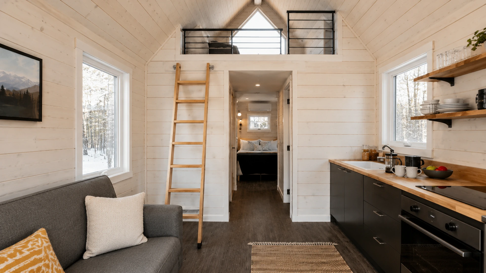 Bright tiny-home interior with a sofa, kitchen and sleeping loft.